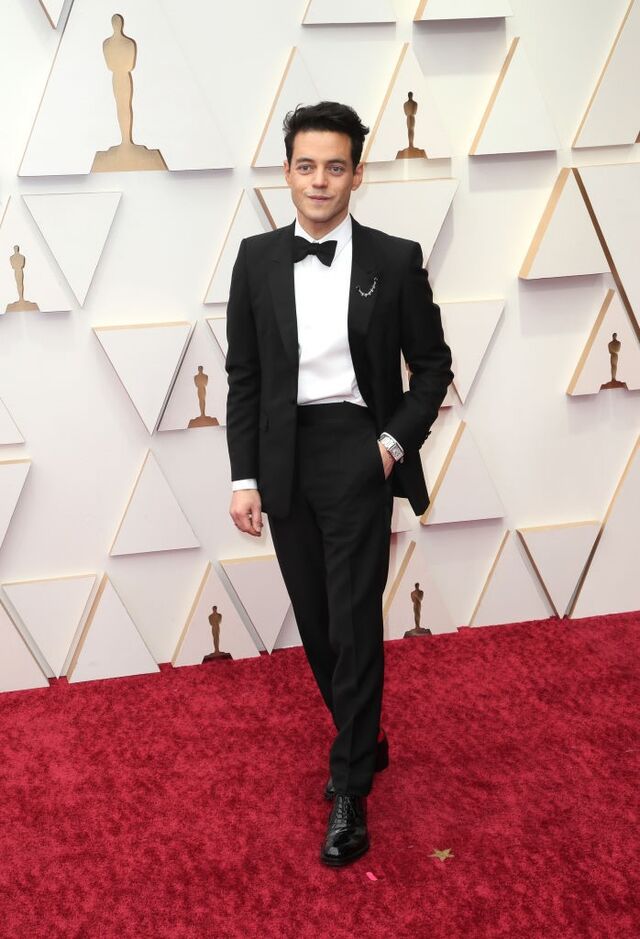 Rami Malek com fato Prada e alfinete e relógio Cartier