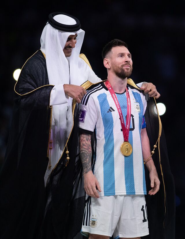 Lionel Messi recebe uma peça tradicional árabe, denominada bisht, do Xeque Tamim bin Hamad Al Thani, Emir do Catar, durante a cerimónia de entrega de prémios após a final da Copa do Mundo da FIFA 2022 no Estádio Lusail, 18 de dezembro de 2022.