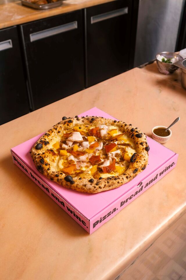 Esta extravagante pizza apresenta uma combinação inesperada de sabores, incluindo porchetta de barriga de porco temperada à moda da Bairrada, laranja, molho de leitão, batata frita, mozzarella fior di latte e bechamel da casa.