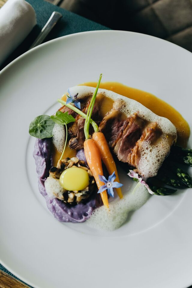 Peito de pato lacado com molho de laranja, puré de batata violeta, duxelle de cogumelos com ovo de codorniz e legumes.
