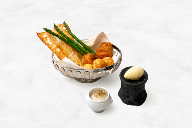 O couvert foge à norma, apresentando um brioche folhado, gougère de comté, torradas de baguete, manteiga com flor de sal, dip de anchovas e espargos (€3,95).