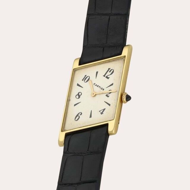 O Cartier Tank Oblique de caixa retangular oblíqua de ouro e bracelete em pele preta.