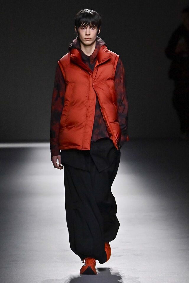 No desfile de Yohji Yamamoto, as peças tinham um ar descomplicado e imponente. As roupas folgadas e largas garantiam conforto, enquanto os tecidos escolhidos—lã axadrezada, algodão macio e veludo rugoso—conferiam textura e caráter ao conjunto. As calças de três quartos, combinadas com polainas volumosas e botas de bico preto, trouxeram uma estética vanguardista.