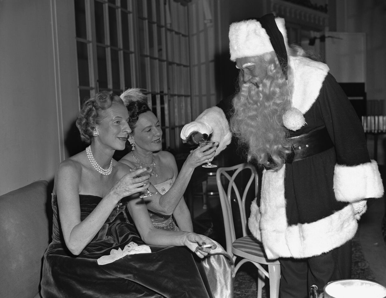 Senhoras brindam com vinho enquanto Pai Natal serve, numa celebração festiva