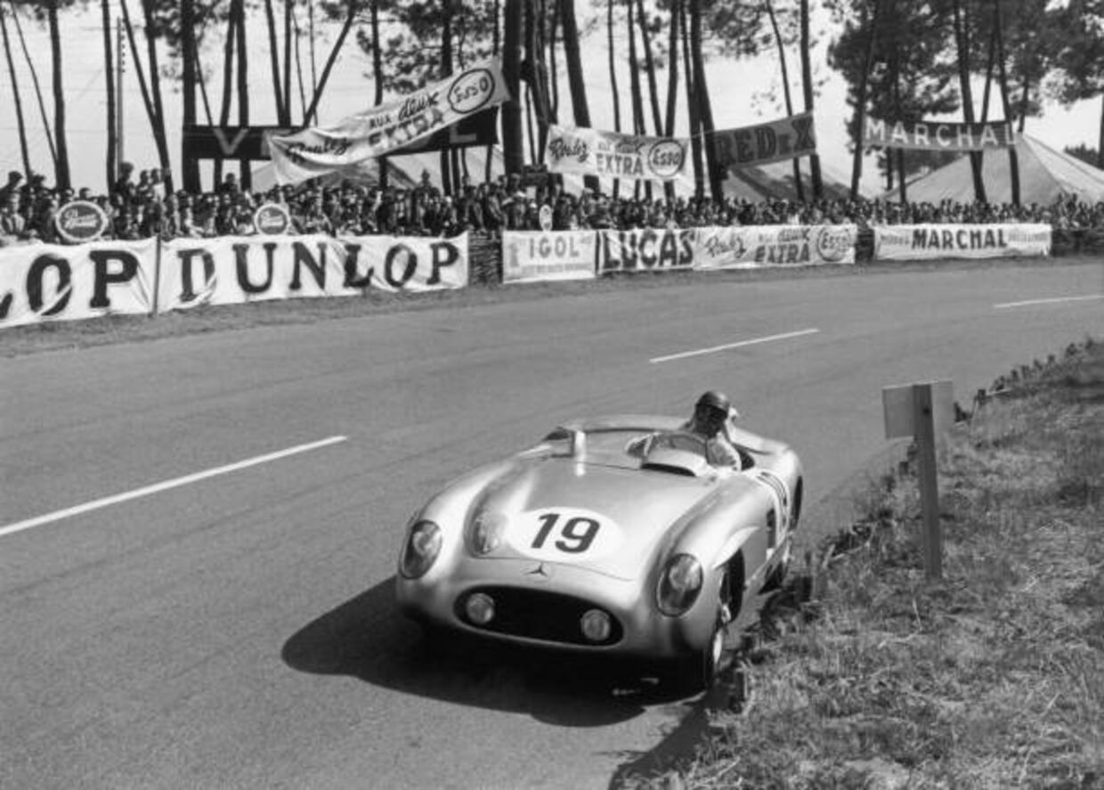 Carro clássico na pista de corrida, com público e marcas nas bancadas